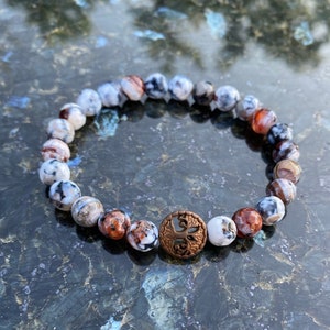 Könnte beinhalten: Ein Armband aus weißen, braunen und roten Achatperlen mit einem Kupferanhänger in Form eines Baumes.