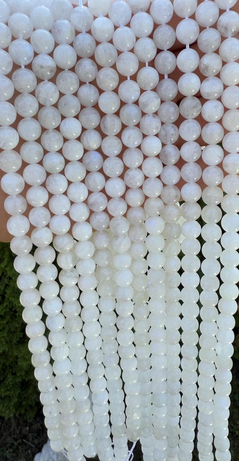 May include: Strands of white, round gemstone beads. The beads have a smooth, polished surface and are strung together. The beads are a milky white color with subtle variations in tone. The beads are a popular choice for jewelry making.