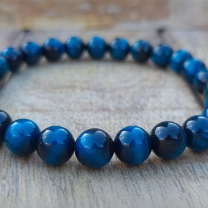 May include: A blue tiger's eye beaded bracelet. The beads are round and have a dark blue colour with a subtle shimmer.