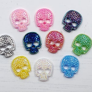 May include: Ten colorful skull-shaped rhinestones with a sparkly finish. The rhinestones are in various colors, including pink, blue, green, silver, and white.