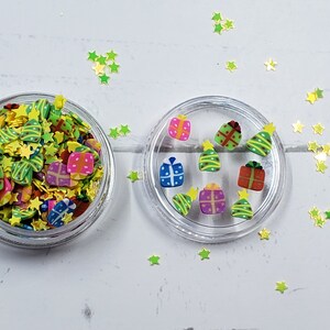 May include: A clear jar filled with colorful Christmas-themed sprinkles, including stars, presents, and Christmas trees. A smaller clear jar with a selection of the same sprinkles is also shown.