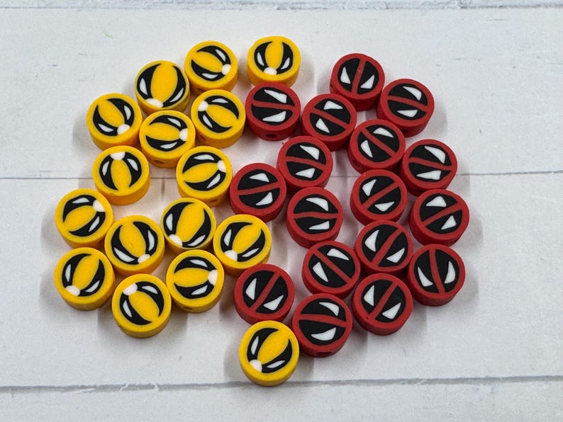 Op de afbeelding: Een verzameling gele en rode ronde kralen. De gele kralen hebben een zwart-wit ontwerp, terwijl de rode kralen een wit-zwart ontwerp hebben. Deze kralen zijn geschikt voor het maken van sieraden en knutselen.