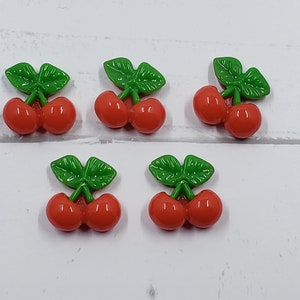 May include: Six red and green cherry shaped buttons. The cherries are a glossy red and the leaves are a bright green.