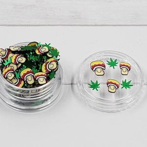 May include: A clear plastic container filled with green and yellow mushroom and leaf shaped glitter. The container has a clear lid with a few mushrooms and leaves on the inside.