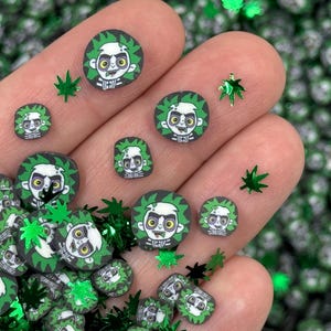 May include: Green and black resin flatback embellishments featuring a cartoon character with a green background. The character has green hair, a green shirt, and a green background. The embellishments are scattered on a hand and a surface.