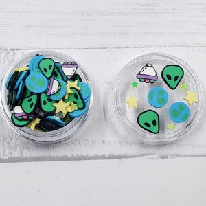 May include: Two clear containers filled with colorful alien-themed charms. The charms include green aliens, spaceships, planets, and stars. The charms are perfect for slime, resin, or other crafts.