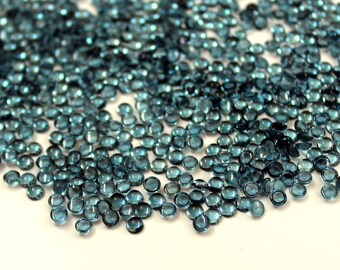 May include: A large pile of small, round, blue gemstones. The gemstones are faceted and have a shiny, reflective surface.