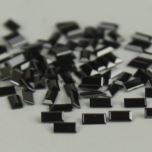 May include: A pile of black rectangular rhinestones, scattered on a white surface.