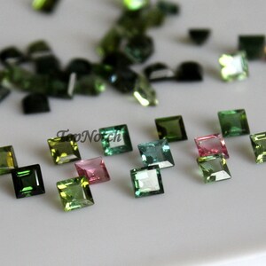 May include: Assortment of green, pink, and blue square-shaped gemstones. The gemstones are faceted and have a shiny finish.