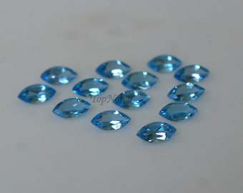 May include: A collection of 15 marquise-shaped, light blue gemstones. The gemstones are scattered on a white surface.
