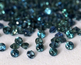 May include: A pile of teal blue gemstones, some of which are scattered on a white surface.