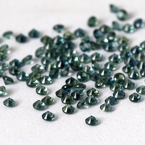 Op de afbeelding: Een strooiing van teal blauwe edelstenen, waarschijnlijk saffieren, op een wit oppervlak. De edelstenen zijn gefacetteerd en hebben verschillende groottes.