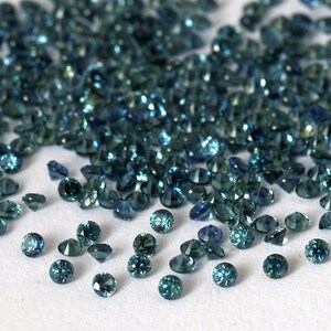 Op de afbeelding: Een hoop losse teal blauwe edelstenen, verspreid over een wit oppervlak.