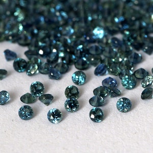 Op de afbeelding: Een hoop losse teal blauwe edelstenen, sommige zijn verspreid over een wit oppervlak.