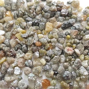 Puede incluir: Una colecci&oacute;n de diamantes en bruto sin cortar en varios tonos de gris, negro y verde. Los diamantes son peque&ntilde;os y tienen una apariencia natural y sin pulir.
