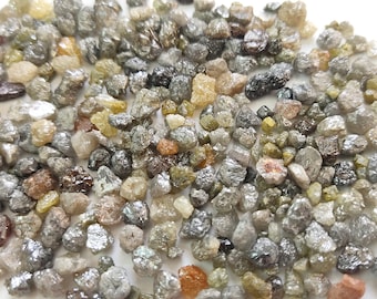 May include: A collection of rough, uncut diamonds in various shades of grey, black, and green. The diamonds are small and have a natural, unpolished appearance.
