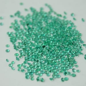 Op de afbeelding: Een grote stapel kleine, ronde, groene edelstenen. De edelstenen zijn verspreid over een wit oppervlak.