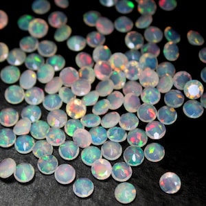 Könnte beinhalten: Eine Sammlung weißer Opal-Edelsteine mit schillernden Regenbogenfarben. Die Edelsteine sind rund und haben eine glatte, polierte Oberfläche.