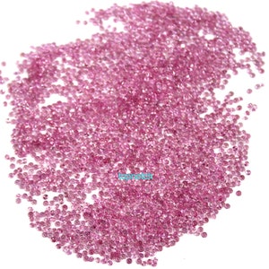 Op de afbeelding: Een grote hoop roze edelstenen, waarschijnlijk robijnen of saffieren, verspreid over een witte achtergrond.