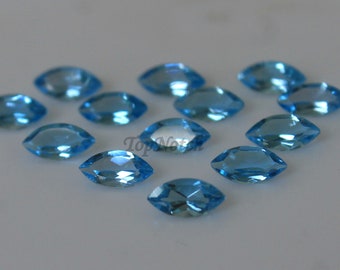 May include: A collection of 12 marquise-shaped, light blue gemstones. The gemstones are arranged in a heart shape on a white surface.