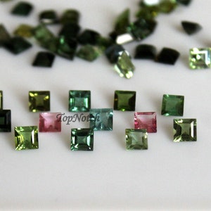 May include: Assortment of green, blue, and pink square-shaped gemstones. The gemstones are arranged in rows on a white surface. Top Notch is written in the lower left corner of the image.