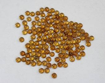 May include: A pile of approximately 100 round, translucent, amber-colored glass cabochons. The cabochons are about 6mm in diameter and have a smooth, polished surface.