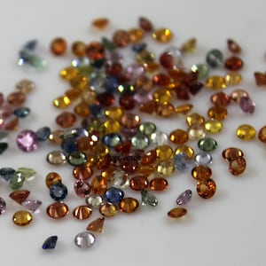 Puede incluir: Una colección de piedras preciosas facetadas sueltas en varios colores, incluidos azul, verde, amarillo, naranja y rojo. Las piedras preciosas son redondas y tienen un acabado pulido.