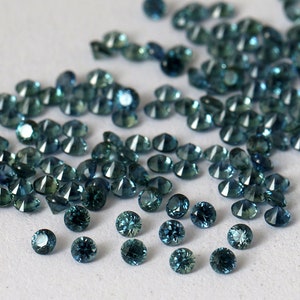 Op de afbeelding: Een losse stapel teal blauwe edelstenen, waarschijnlijk saffieren, op een wit oppervlak.