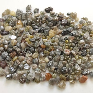 Puede incluir: Un mont&oacute;n de peque&ntilde;os diamantes en bruto grises, marrones y verdes. Los diamantes son de varias formas y tama&ntilde;os.