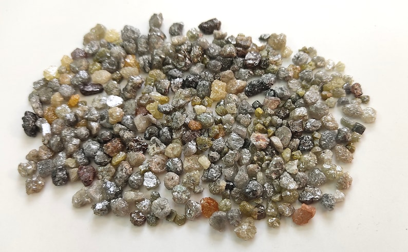 Puede incluir: Un mont&oacute;n de peque&ntilde;os diamantes en bruto grises, marrones y verdes. Los diamantes son de varias formas y tama&ntilde;os.