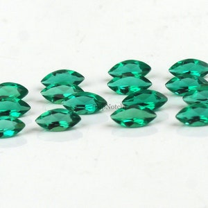 May include: A group of 12 marquise-shaped green gemstones. The gemstones are faceted and have a brilliant shine.