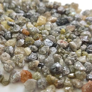Puede incluir: Primer plano de un mont&oacute;n de peque&ntilde;os diamantes en bruto grises, verdes y marrones. Los diamantes son de diversas formas y tama&ntilde;os.