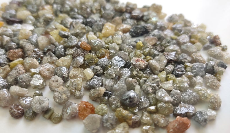 Puede incluir: Primer plano de un mont&oacute;n de peque&ntilde;os diamantes en bruto grises, verdes y marrones. Los diamantes son de diversas formas y tama&ntilde;os.