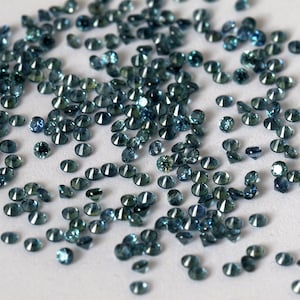 Op de afbeelding: Een strooiing van teal blauwe edelstenen op een wit oppervlak. De edelstenen zijn rond en hebben een facetgeslepen.