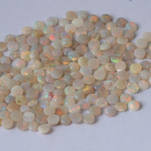 Puede incluir: Un montón de cuentas de piedra preciosa de ópalo blanco con colores arcoíris iridiscentes. Las cuentas son redondas y lisas, y son perfectas para hacer joyas.