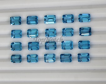 May include: A collection of 18 light blue, rectangular, faceted gemstones arranged in rows on a white surface.