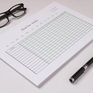 May include: A white Plant Care Tracker notepad with a green grid, black text, and a black pen. The notepad has a title and checkboxes for water and feed. Black glasses rest on the top left.