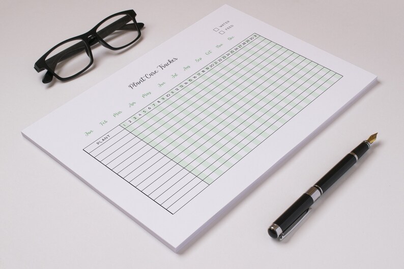 May include: A white Plant Care Tracker notepad with a green grid, black text, and a black pen. The notepad has a title and checkboxes for water and feed. Black glasses rest on the top left.