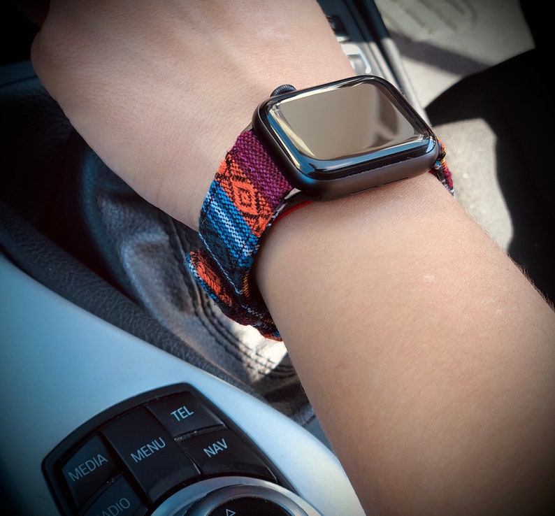 May include: A black smartwatch with a colorful patterned band featuring orange, blue, and purple geometric designs. The watch is worn on a wrist, showcasing the band's intricate details and the watch's sleek, modern design.
