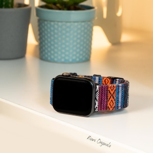 May include: Black smartwatch with a patterned band in blue, orange, purple, and white. The band has a woven design. The watch is on a white surface. The text "Niani Originals" is at the bottom.