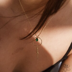 May include: A gold necklace with a green gemstone pendant and a dagger charm hanging from a circle.