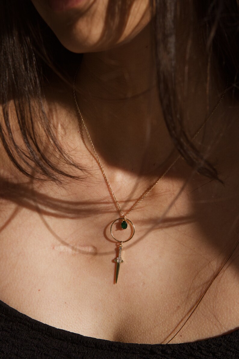 May include: A gold chain necklace with a green gemstone pendant and a small sword charm.