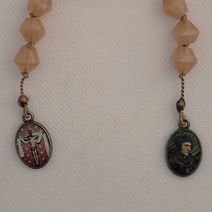 May include: A brown rosary with a crucifix and a saint medal. The rosary beads are made of glass and have a faceted design.