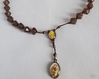 May include: A brown rosary necklace with a brown and gold pendant featuring a religious image. The beads are faceted and have a translucent appearance.