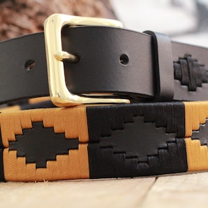 May include: Black leather belt with a gold-coloured buckle. The belt has a woven pattern in black and tan. A stylish accessory for everyday wear, this belt is suitable for various outfits.