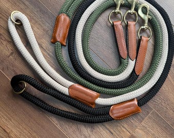 May include: A collection of dog leashes in various colors, including black, olive green, and cream. Each leash is made of thick, braided rope and features a leather accent and a brass-colored clasp and ring.