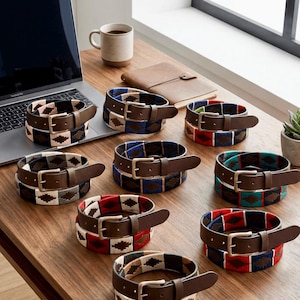 May include: Several leather belts with patterned fabric inlays. The belts have brown leather straps and silver-coloured buckles. The fabric inlays display geometric patterns in various colours, including red, blue, and green.