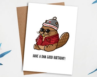 May include: A birthday card featuring a cartoon beaver wearing a red and black plaid shirt, sunglasses, and a toque with a Canadian flag. The text on the card reads "Have a dam good birthday!"