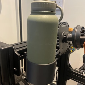 May include: A green water bottle with a black holder attached to a 3D printer.