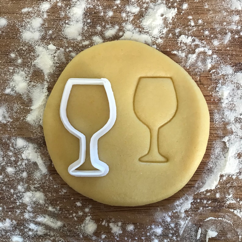 Puede incluir: Un cortador de galletas de pl&aacute;stico blanco en forma de copa de vino sobre una superficie marr&oacute;n claro.
